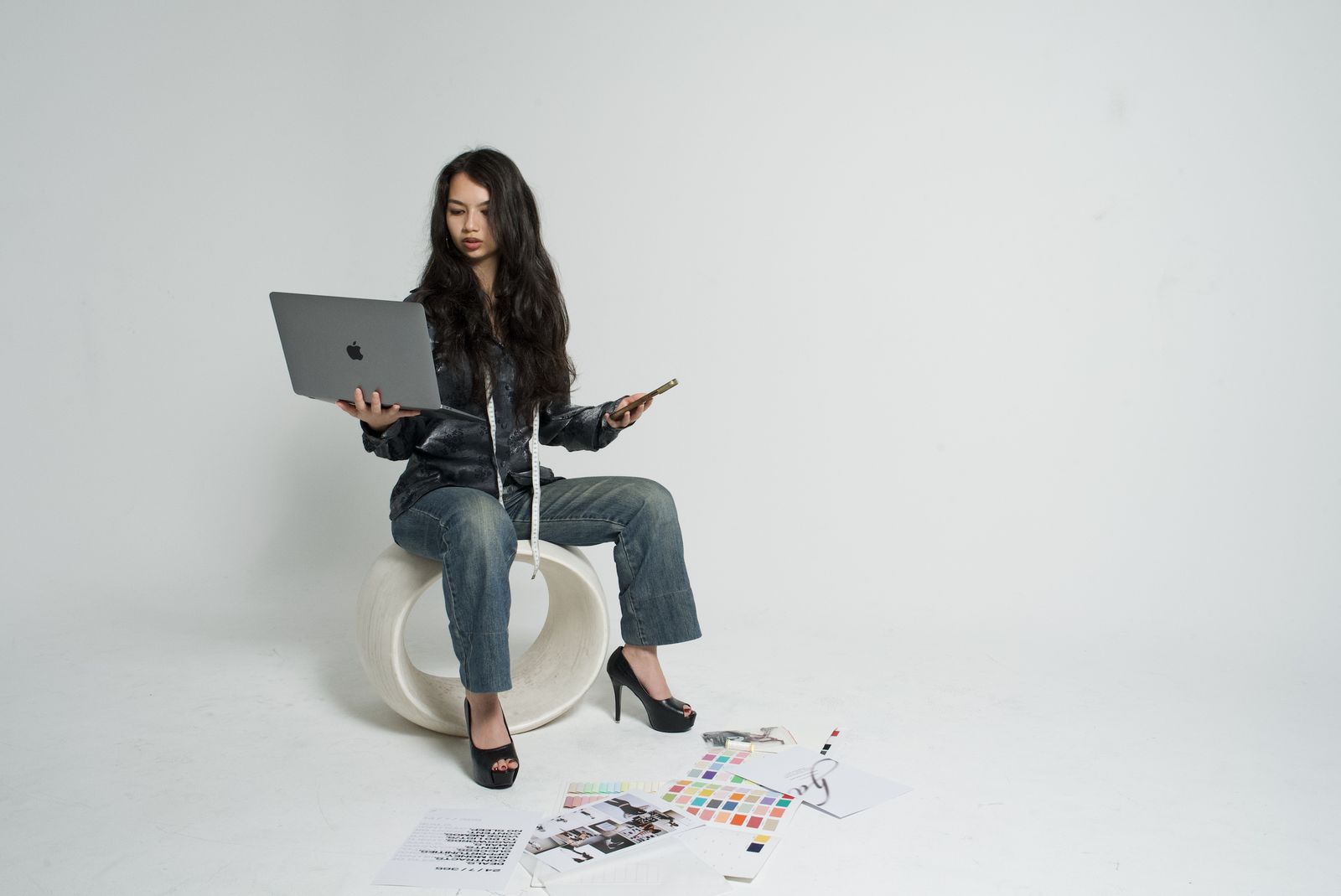 Harmony seated on a sculptural stool with a laptop and phone, swatches at her feet